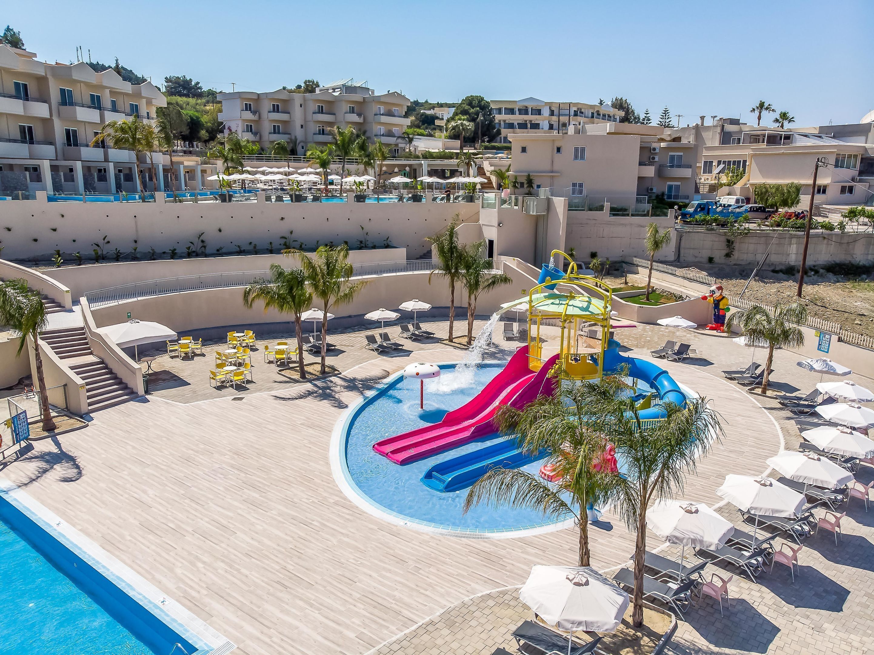 A resort pool area with a water slide, lounge chairs, and umbrellas.