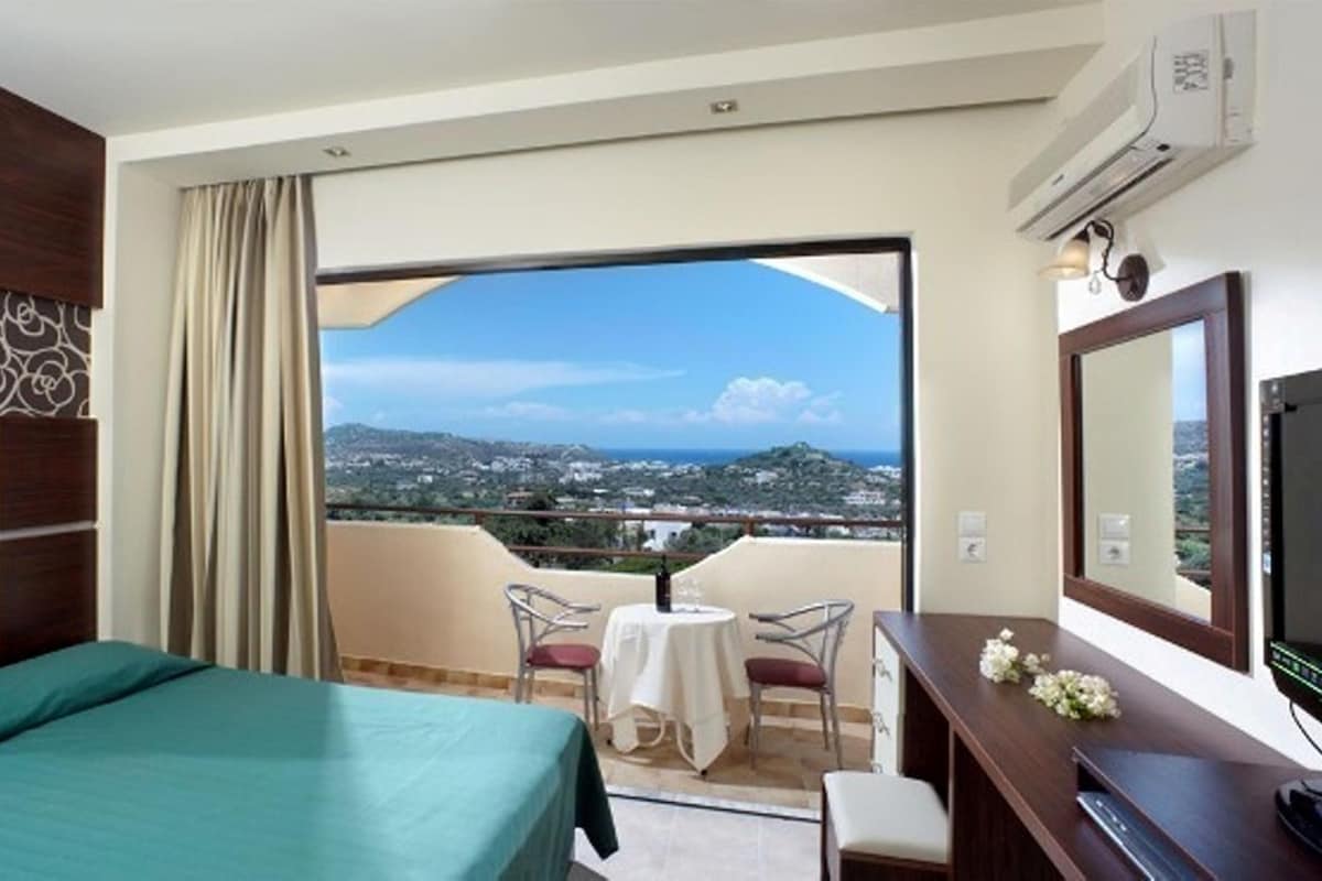 A hotel room with a balcony, a bed, a desk, and a TV.