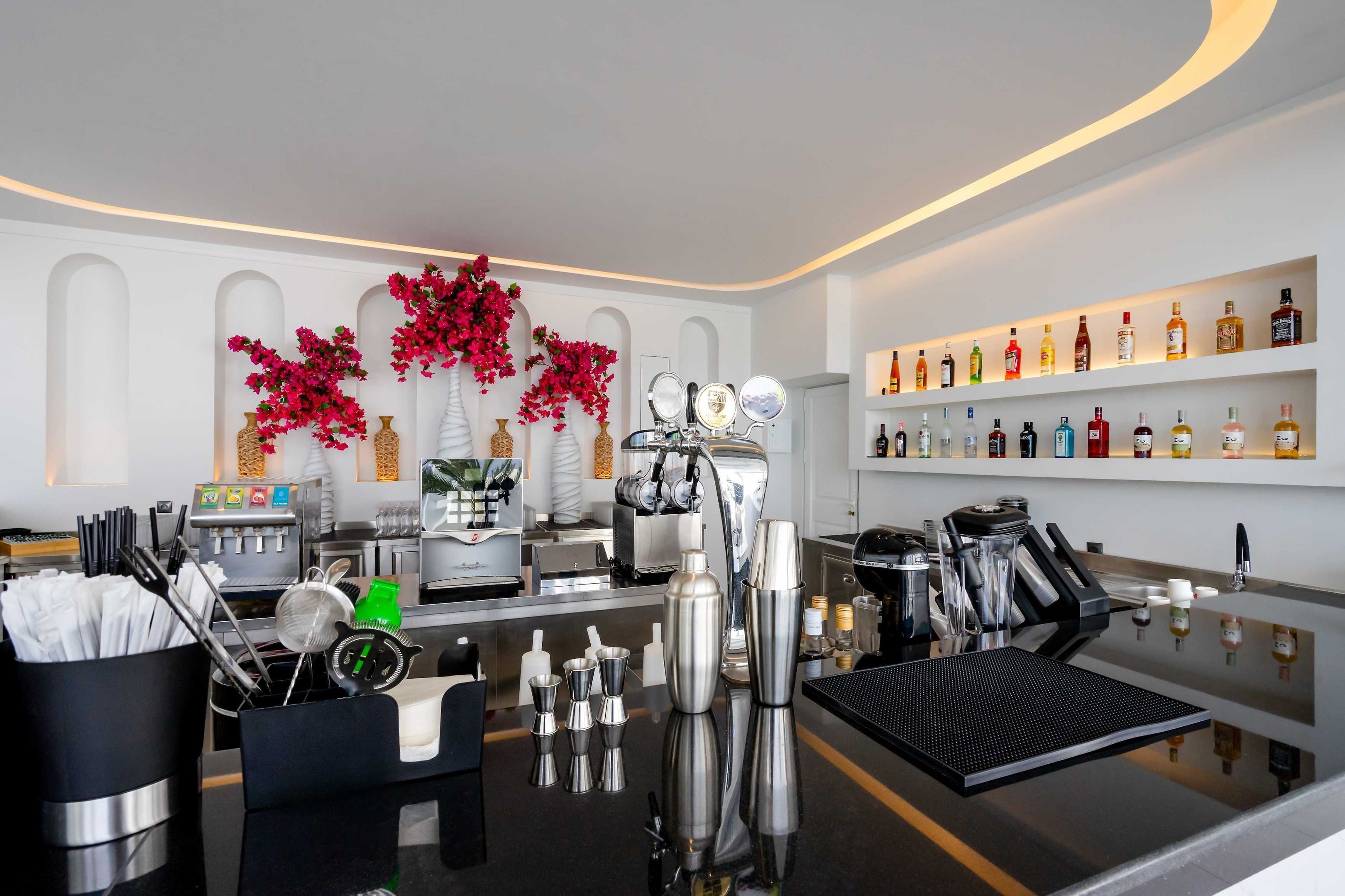 A bar area with a polished counter, bar tools, and a variety of liquor bottles on shelves.