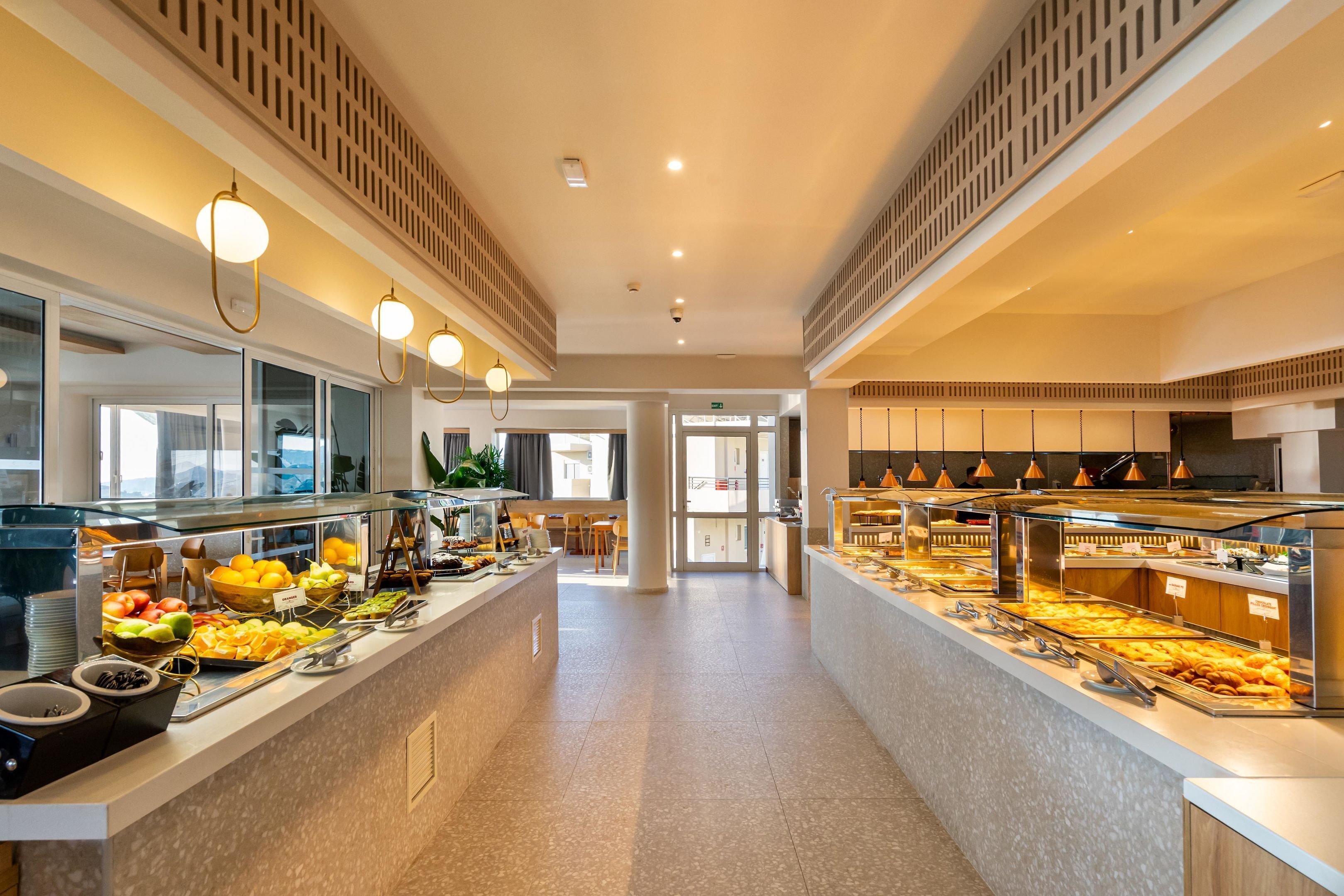Un moderno vestíbulo de hotel con un área de bufé que ofrece diversas opciones de comida y un espacio de descanso con mesas y sillas.