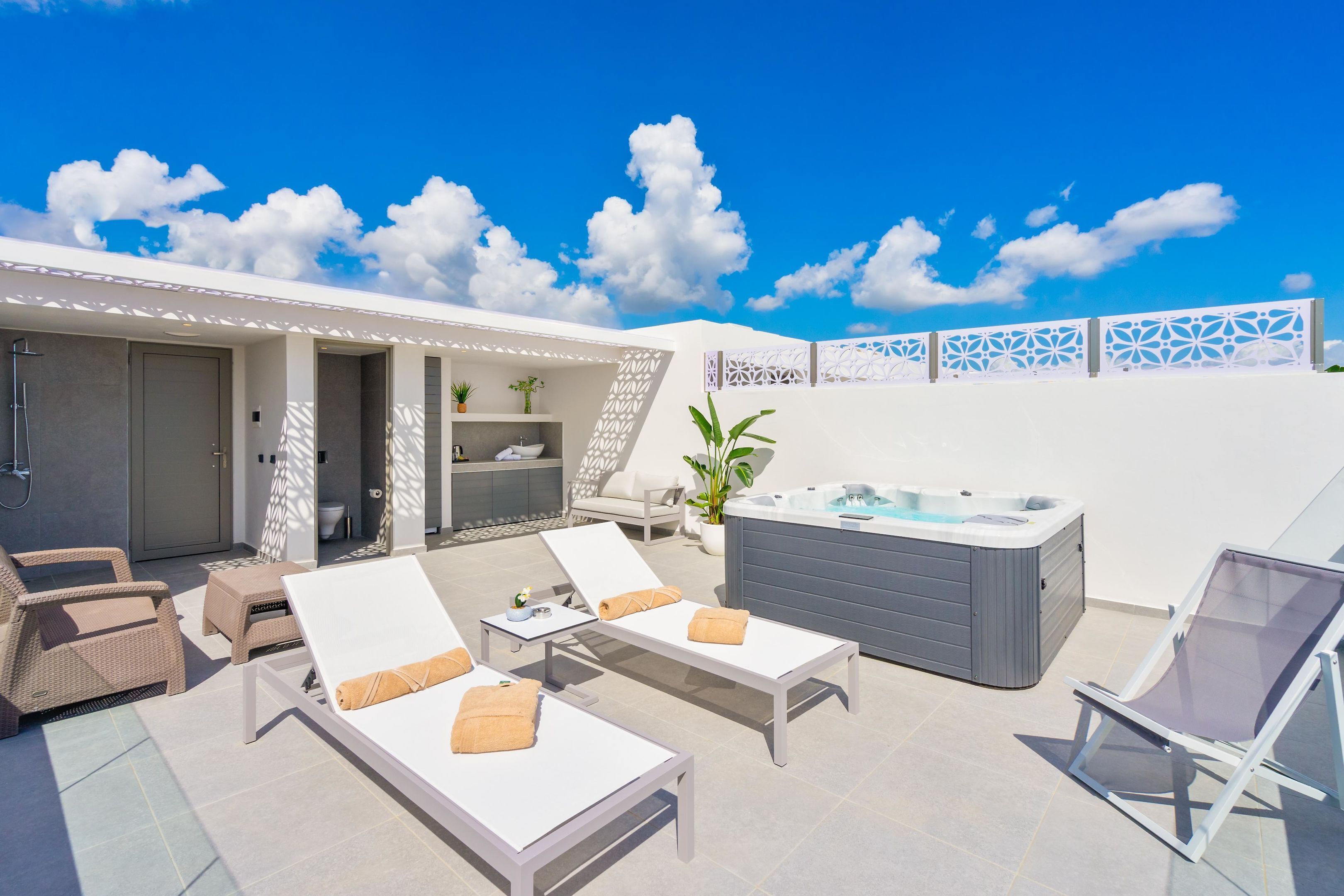 A rooftop terrace with lounge chairs, a hot tub, and a view of the sky.