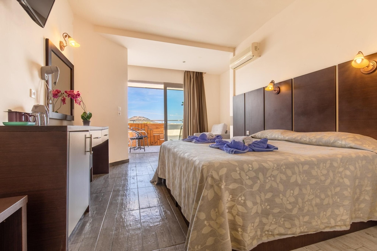 A hotel room with a bed, a desk, a chair, and a view of the outdoors.