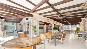 Un'ampia sala da pranzo interna con tavoli e sedie in legno, una parete decorativa in pietra e lampade pendenti.