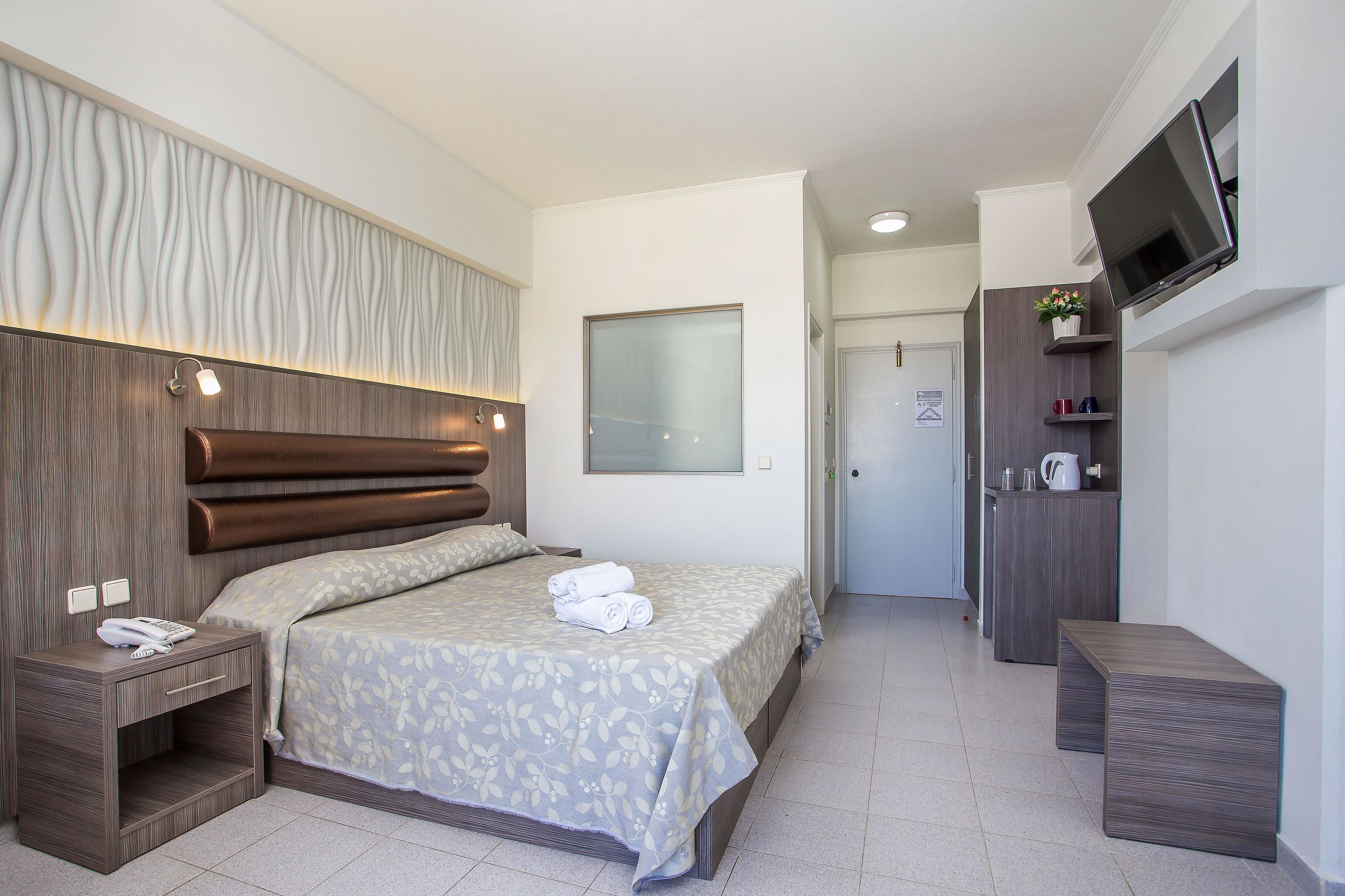Une chambre d’hôtel équipée d’un lit, d’une table de chevet et d’un téléviseur fixé au mur.