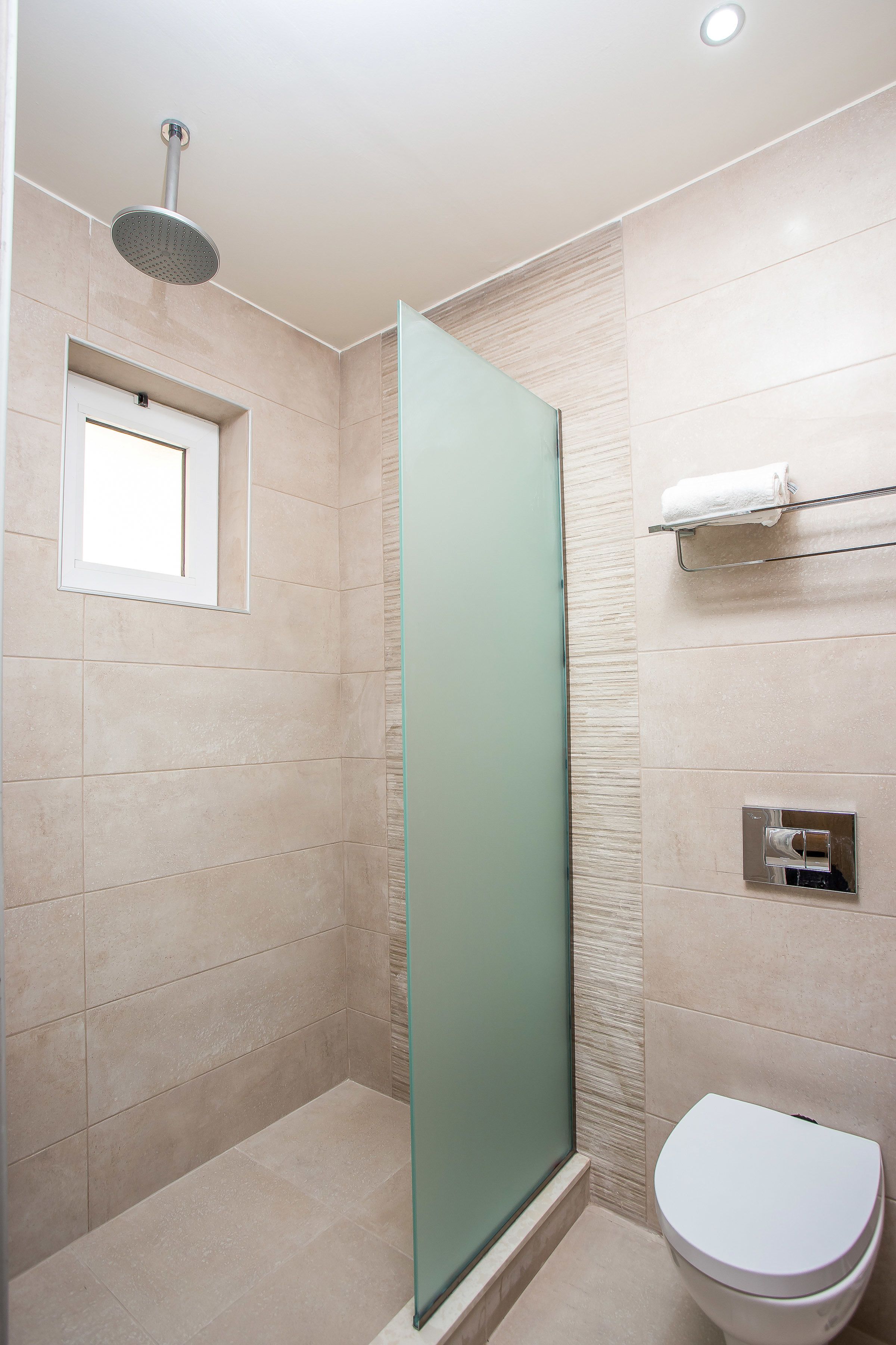 Een moderne badkamer met een douchecabine van glas, een toilet en een handdoekrek.