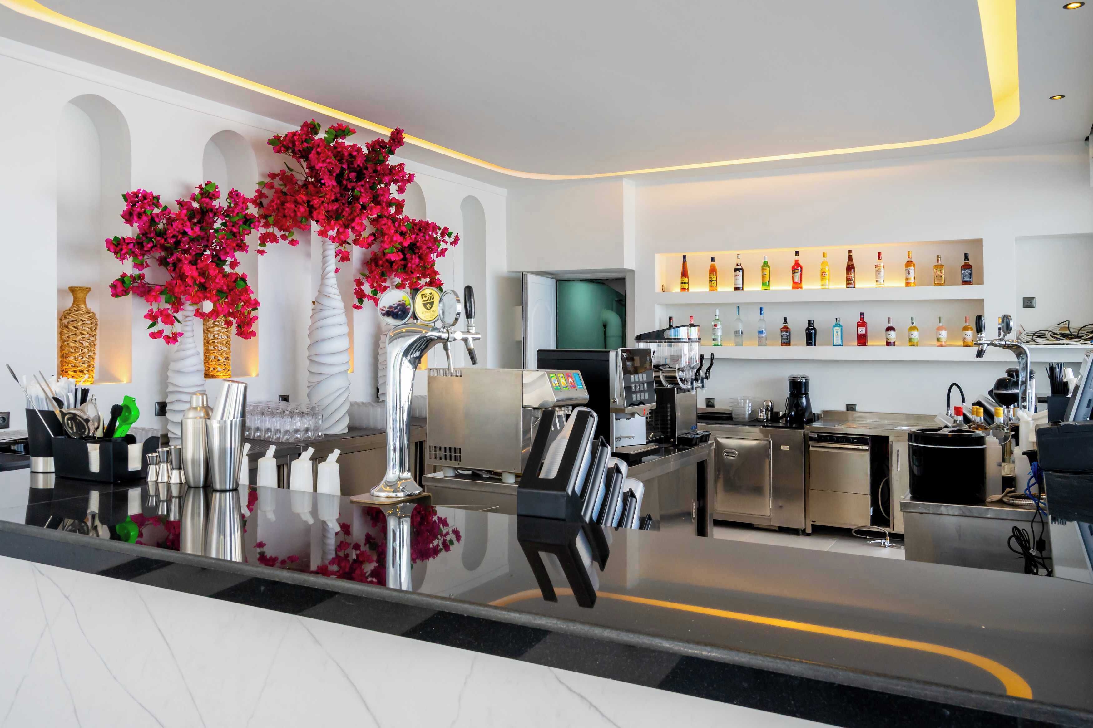 Zona de bar moderna con una barra elegante, una variedad de botellas de licor y un arreglo floral decorativo.
