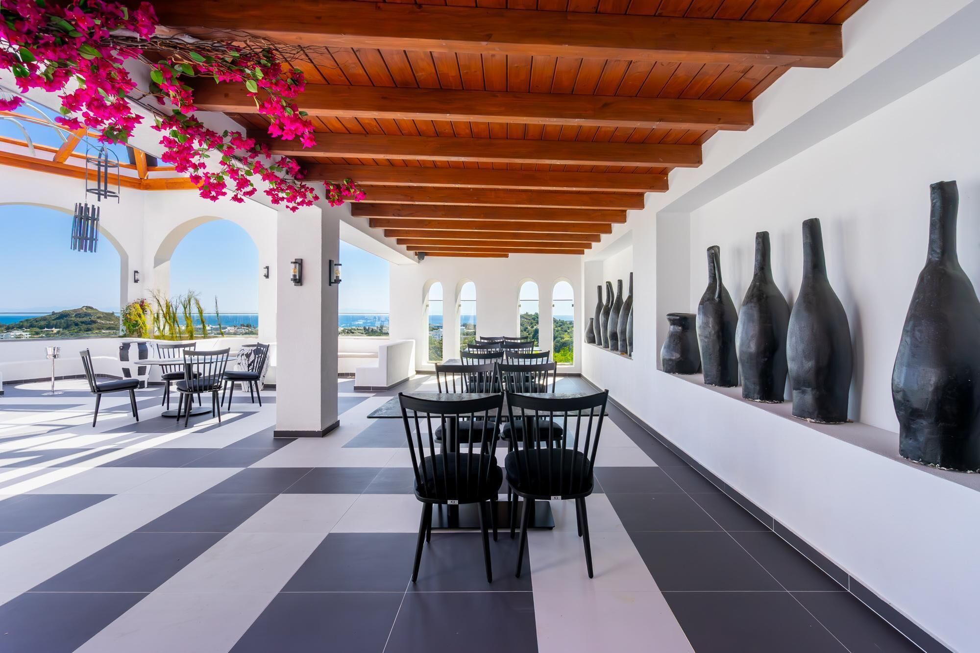 A terrace with black and white checkered flooring, wooden ceiling beams, and black chairs.