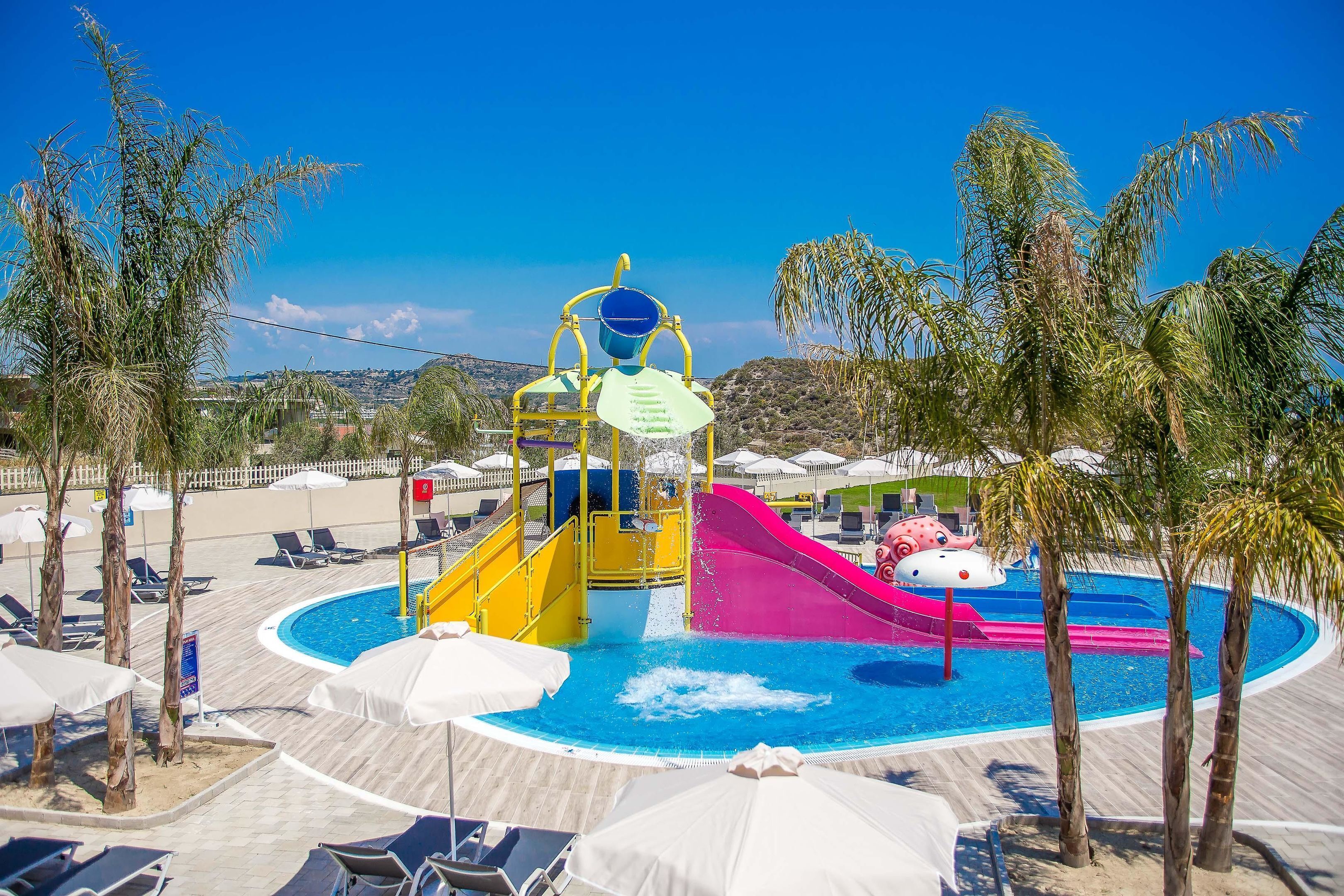 A water park with slides and a pool, surrounded by palm trees and lounge chairs.