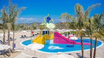 A water park with slides and a pool, surrounded by palm trees and lounge chairs.