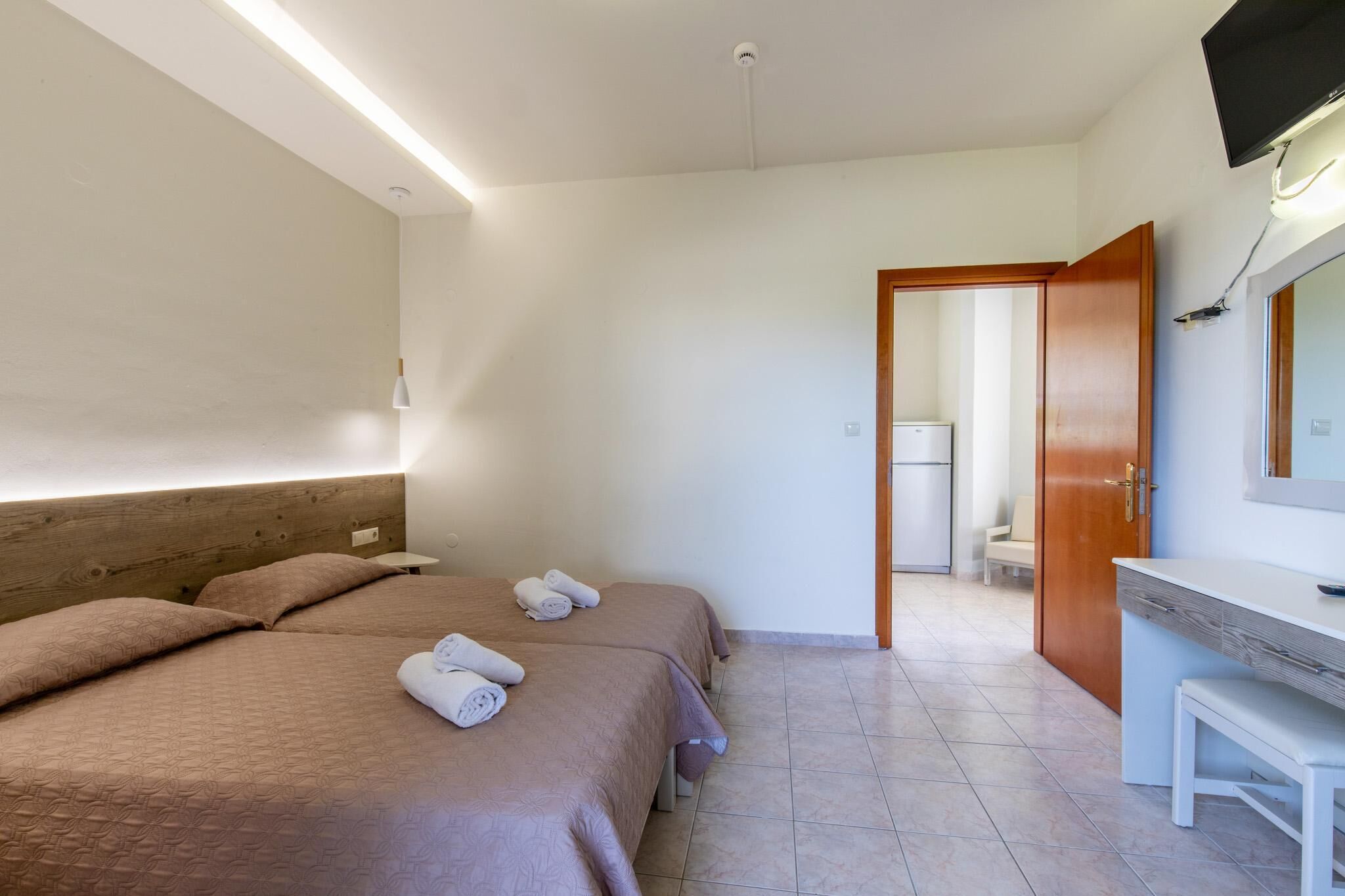 A hotel room with two beds, a wooden headboard, a white desk, and a bathroom visible through an open door.