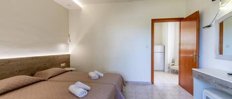 A hotel room with two beds, a wooden headboard, a white desk, and a bathroom visible through an open door.