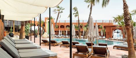 A poolside area with sun loungers, umbrellas, and palm trees.