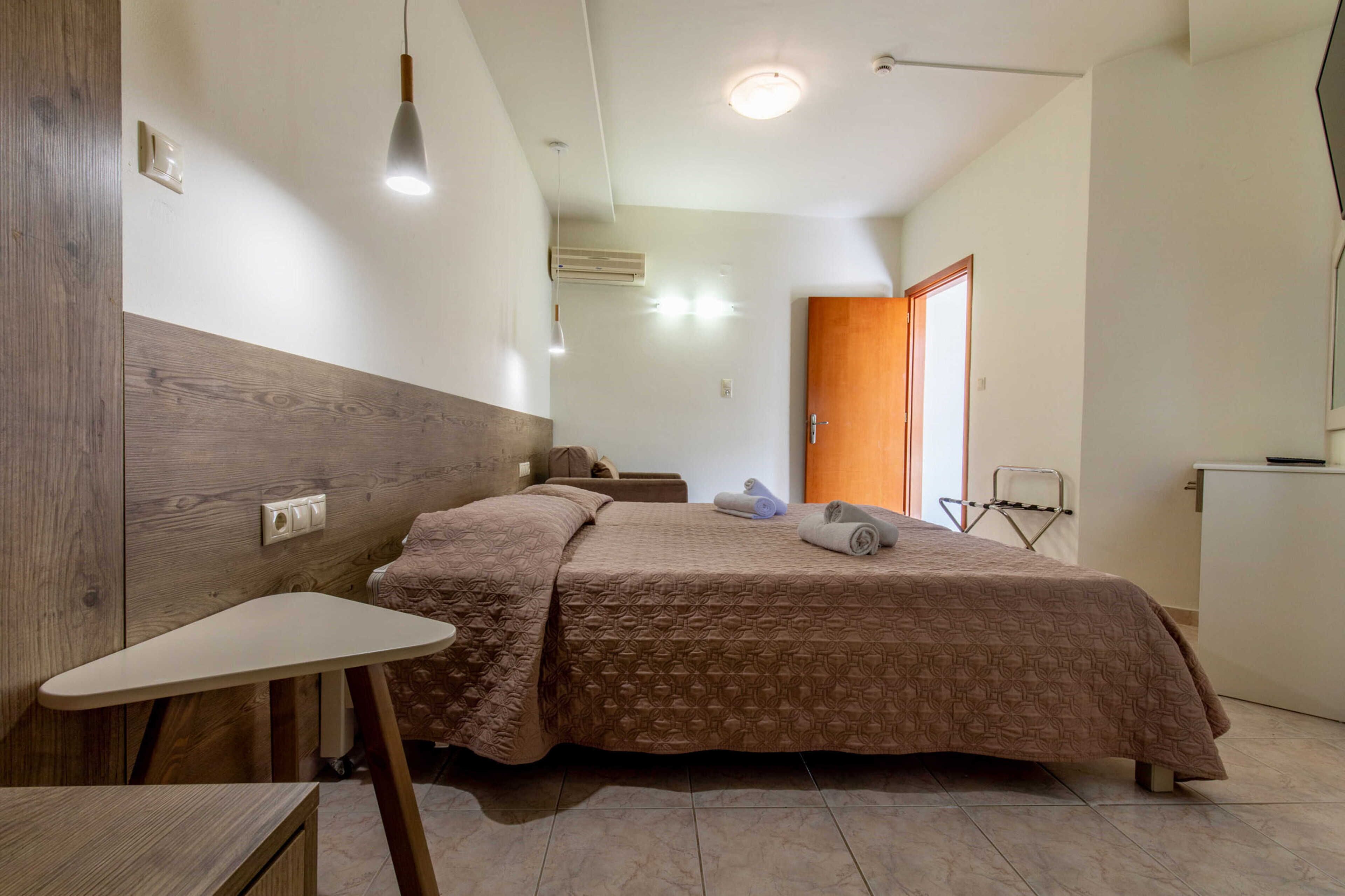 Quarto com cama, mesa de cabeceira, abajur e porta para outro cômodo.