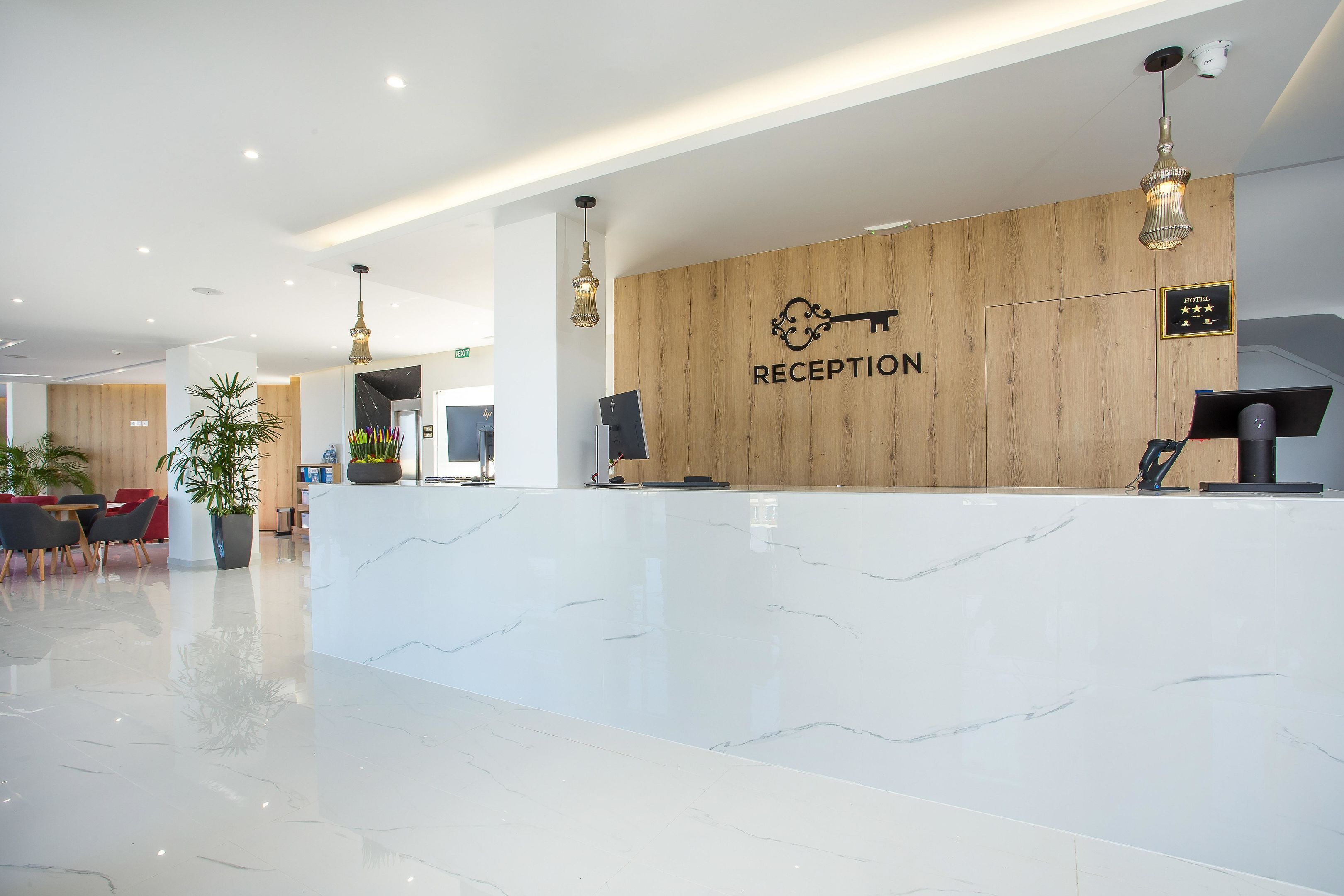 A hotel reception area with a marble counter, wooden paneling, and modern lighting fixtures.