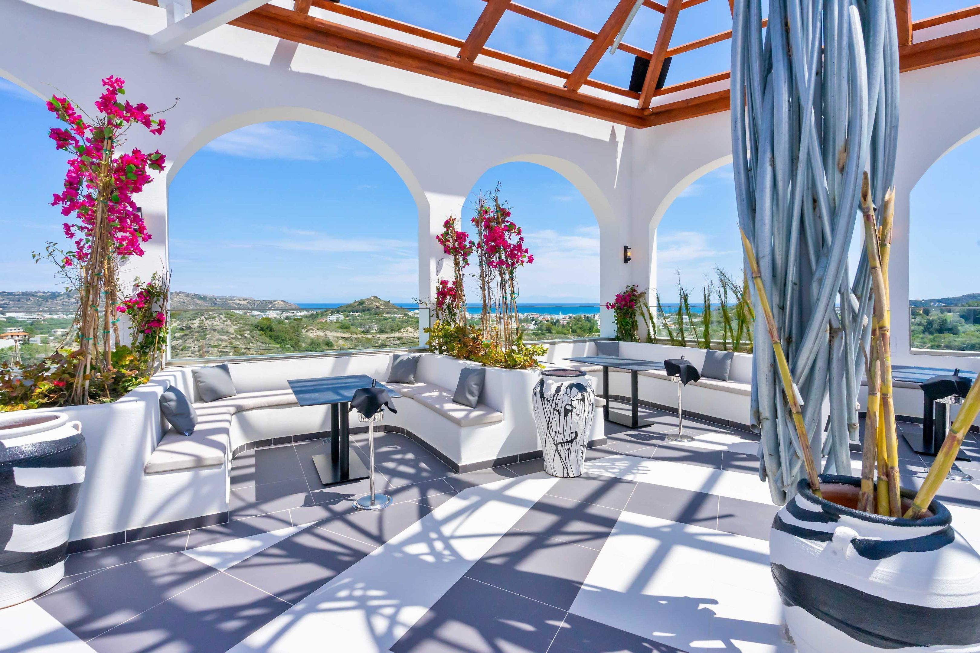 Une terrasse sur le toit, avec des canapés blancs, une table à manger et des plantes en pot.
