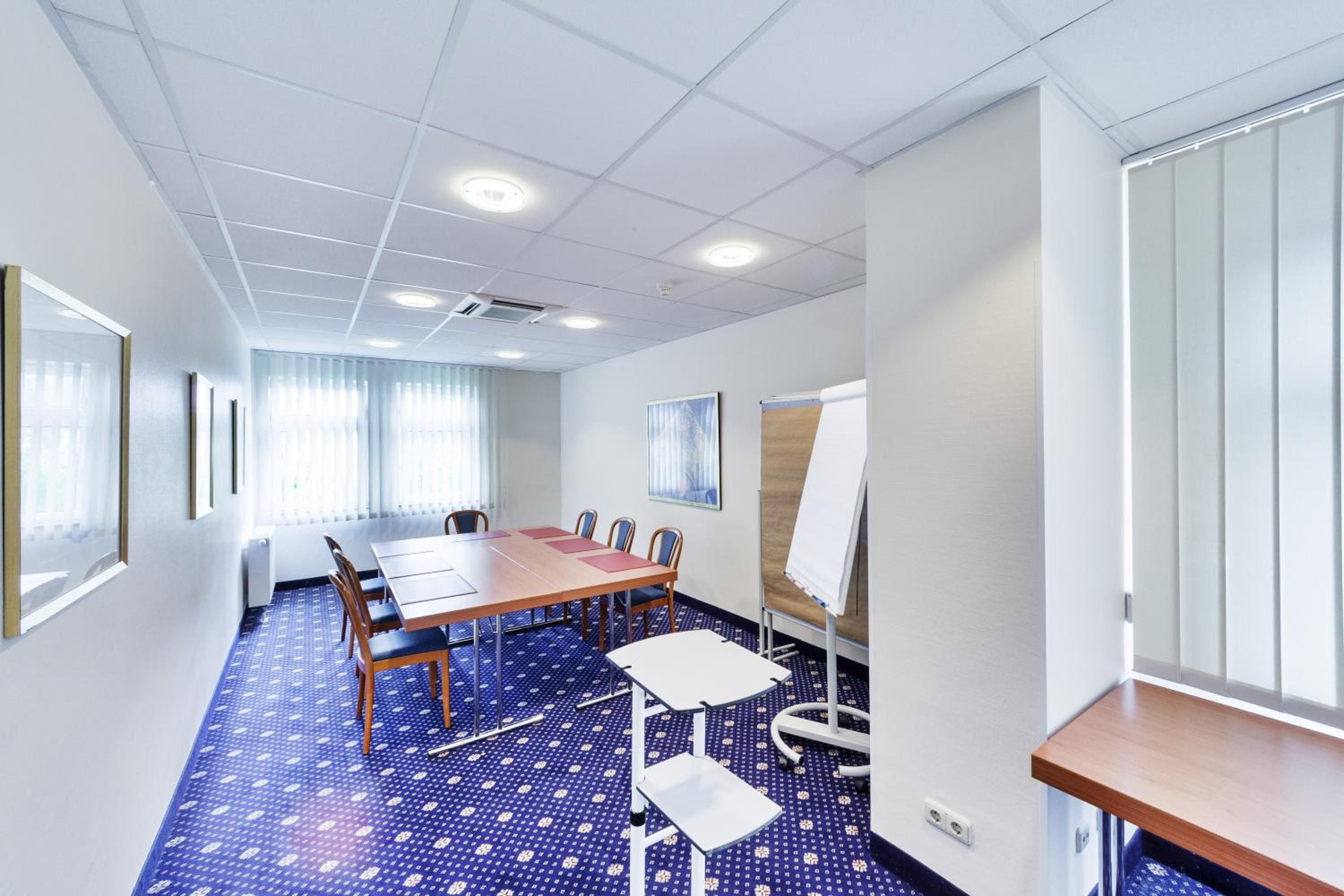 A conference room with a long table, chairs, a whiteboard, and a patterned carpet.