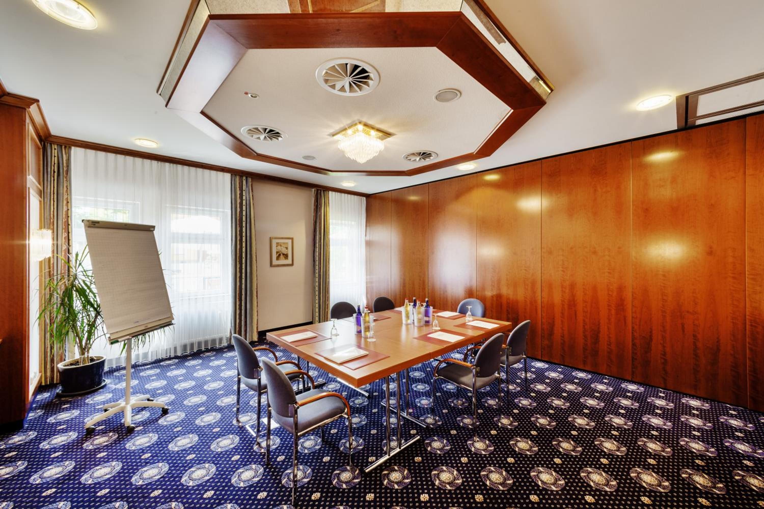 Une salle de conférence avec une table en bois, des chaises, un tableau blanc et un tapis à motifs.