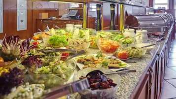 Un bufé con diversos platos, entre ellos ensaladas, frutas y carnes.
