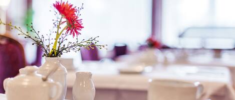 Uma mesa com uma chaleira branca, um pequeno vaso com uma flor e uma xícara e pires.
