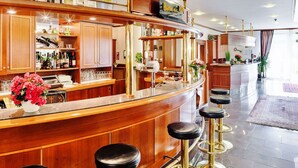 A bar area with wooden cabinets, a bar counter, stools, and a variety of bottles and glasses. - Trans World Hotel Columbus (Seligenstadt)