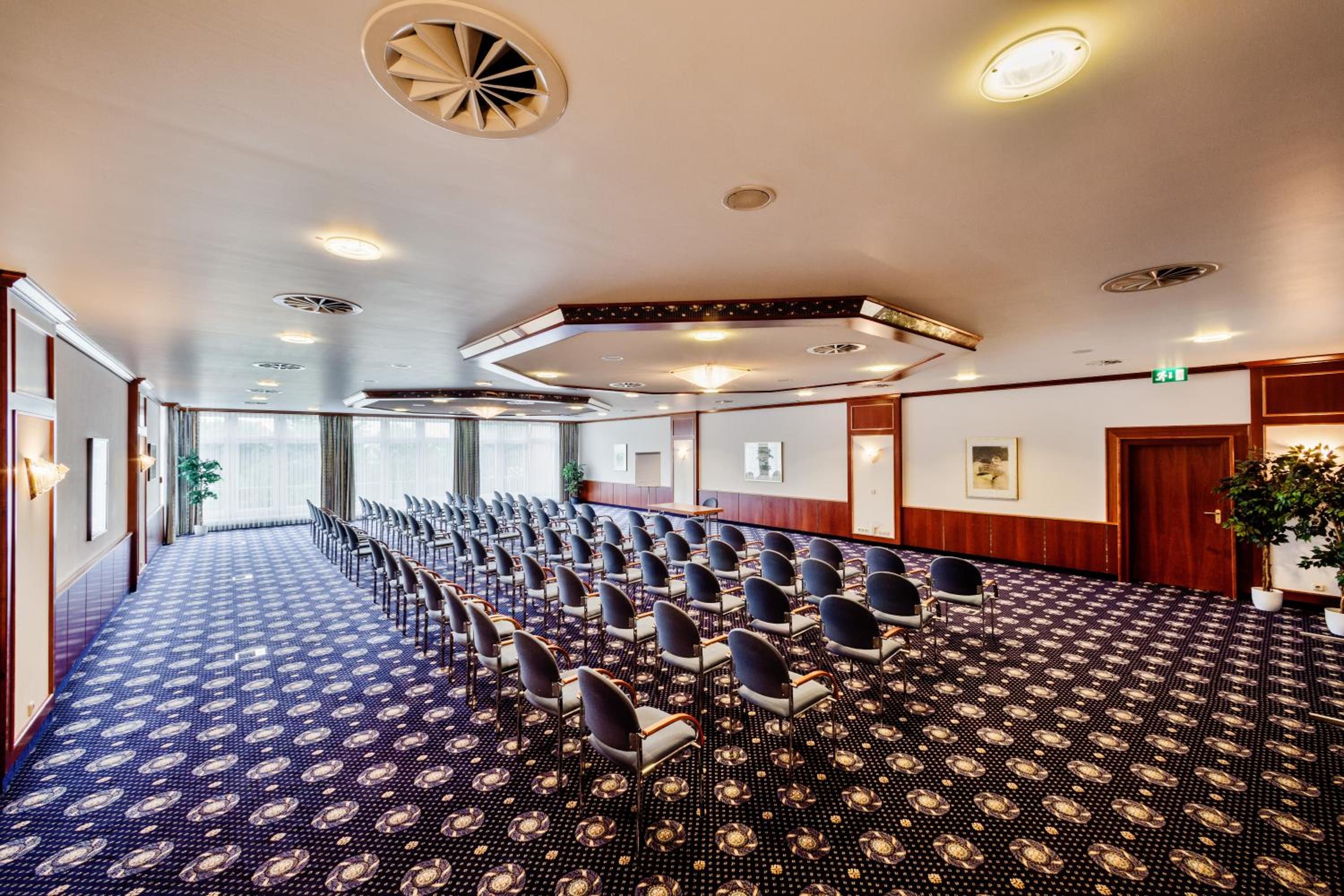 Ein Konferenzraum mit Reihen von Stühlen, einem gemusterten Teppich und Deckenleuchten.
