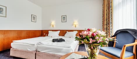 Una habitación de hotel con cama, una silla, una mesa con un jarrón de flores y lámparas fijadas a la pared.