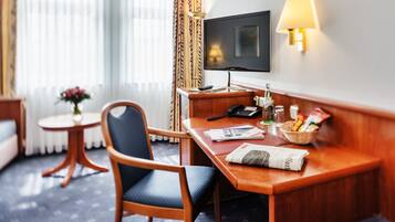 Een hotelkamer met een houten bureau, een stoel, een televisie, een lamp en een tafeltje met een bloemenvaas.