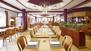 A spacious dining area with long tables, chairs, and a central decorative plant. - Trans World Hotel Columbus (Seligenstadt)