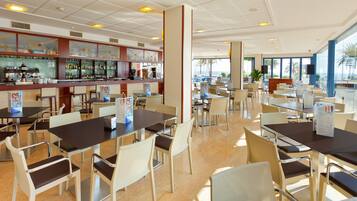 Un restaurant spacieux, doté de nombreuses tables et chaises, d’un bar bien garni et de grandes fenêtres offrant une vue panoramique.