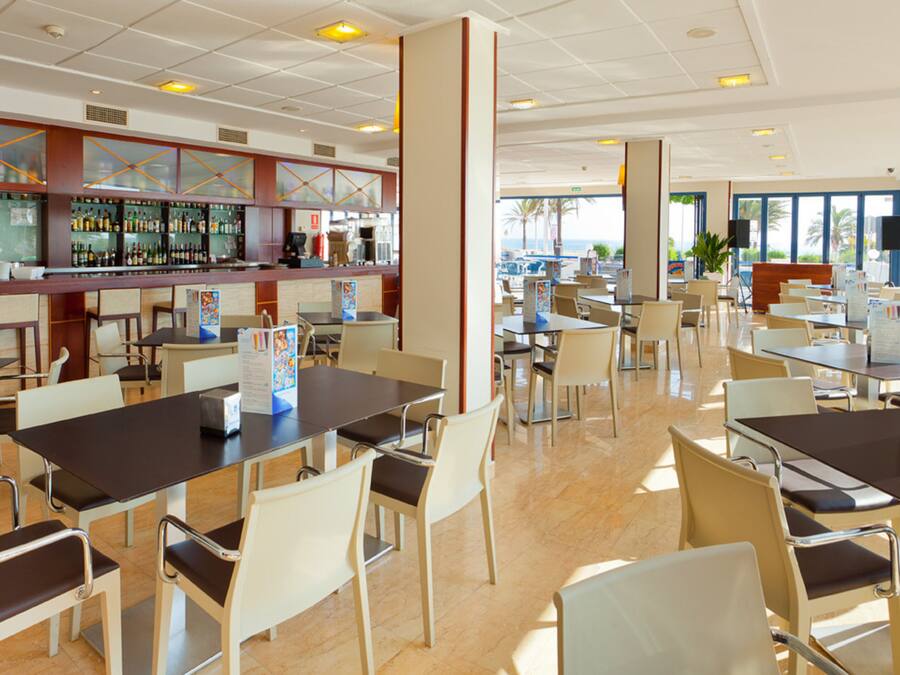 Un restaurant spacieux, doté de nombreuses tables et chaises, d’un bar bien garni et de grandes fenêtres offrant une vue panoramique.