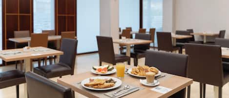 A modern dining area with tables and chairs, breakfast plates, and a glass of orange juice.