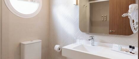 A modern bathroom with a round window, a toilet, a sink with a mirror, and a hairdryer on the wall.