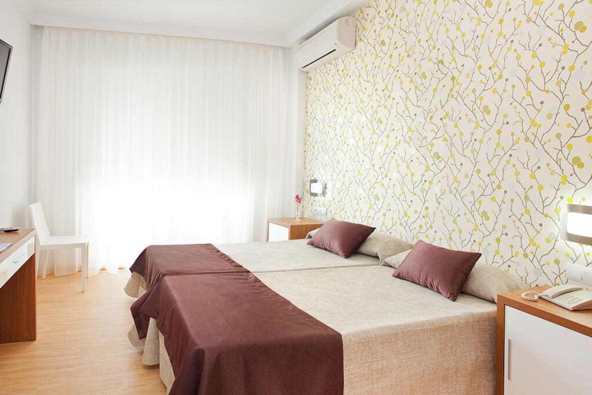 Una habitación de hotel con cama, escritorio, silla, televisor y papel tapiz estampado.