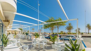 An outdoor cafe with white tables and chairs, a covered seating area, and a view of the sea. - Hotel RH Riviera -  Recommended for Adults By Hoteles RH (Gandia)