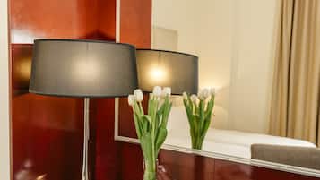 A hotel room with a glass desk, a lamp, a vase with white flowers, a magazine, and a cup.
