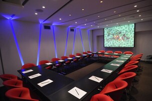 Una sala conferenze con un lungo tavolo, sedie rosse e uno schermo proiettore che mostra un motivo.