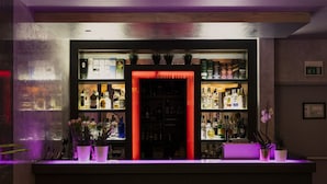 A bar area with shelves of liquor bottles, a red-lit door, and potted plants. - Hotel Cosmopolitan (Florence)
