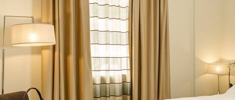 A hotel room with a bed, a sofa, a table with a tray of breakfast, a lamp, and curtains.