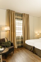 Una camera d'albergo con un letto, un divano, un tavolo con un vassoio per la colazione, una lampada e tende.