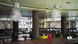 A restaurant interior with wooden tables, hanging light fixtures, and a bar area in the background. - Room Mate Alicia, Madrid (Madrid)