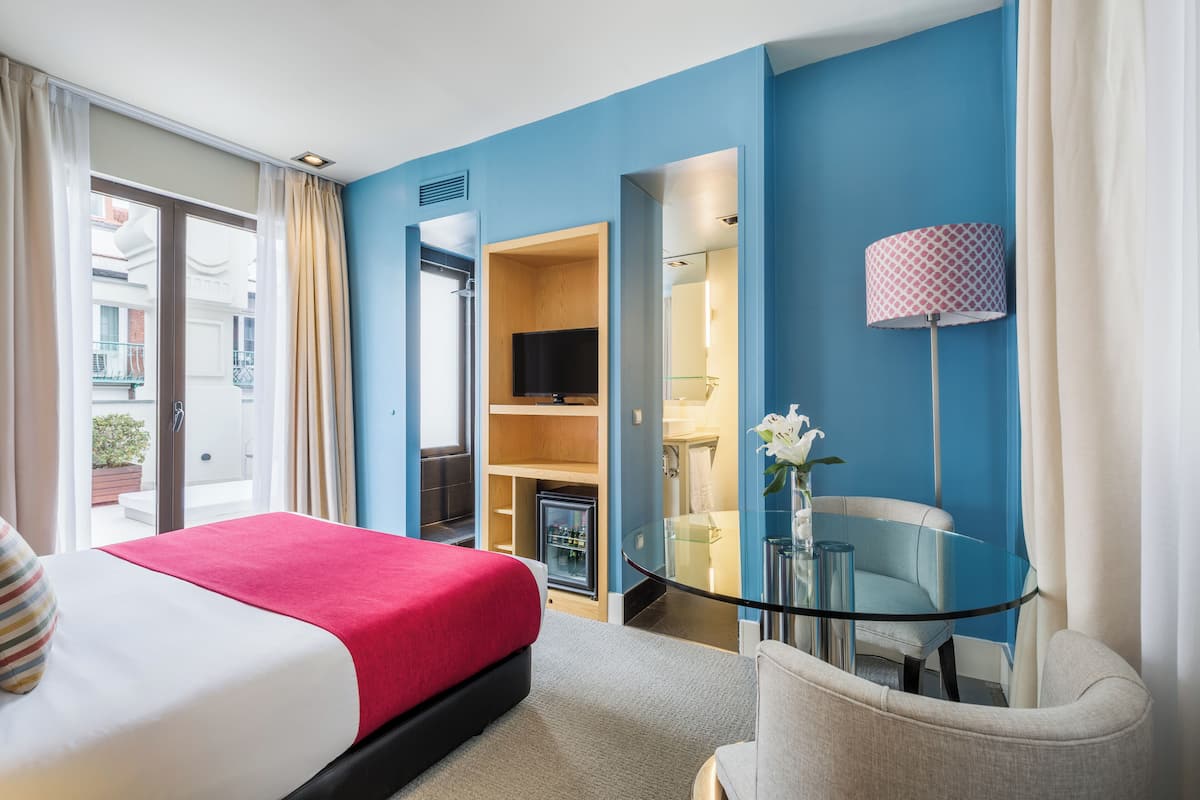 A hotel room with a bed, a glass table, a TV, a wardrobe, and a balcony view.