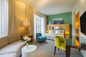 Ein Hotelzimmer mit einem Bett, einem Sofa, einem Sessel, einem kleinen Tisch mit einer Vase und einem Fernseher.