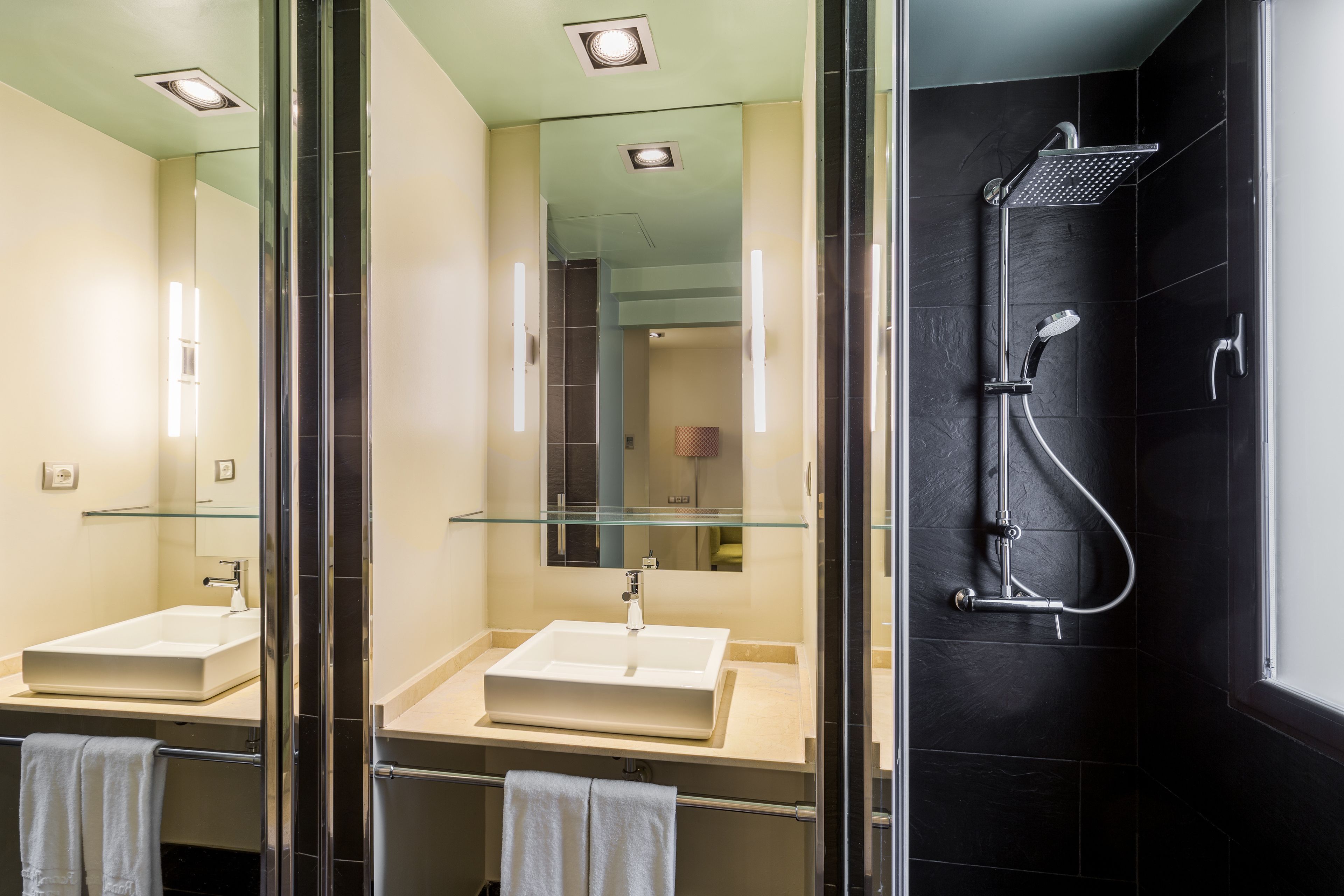 Une salle de bain moderne avec une douche à parois de verre, un grand miroir et un lavabo blanc.