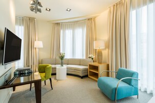 Hotellihuone, jossa on taulutelevisio, sohva, kaksi nojatuolia, sohvapöytä ja lamppu.