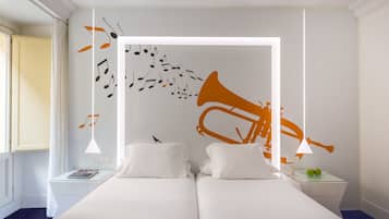 Quarto de hotel com uma cama, mesa de cabeceira, abajur e decoração de trompete com notas musicais.