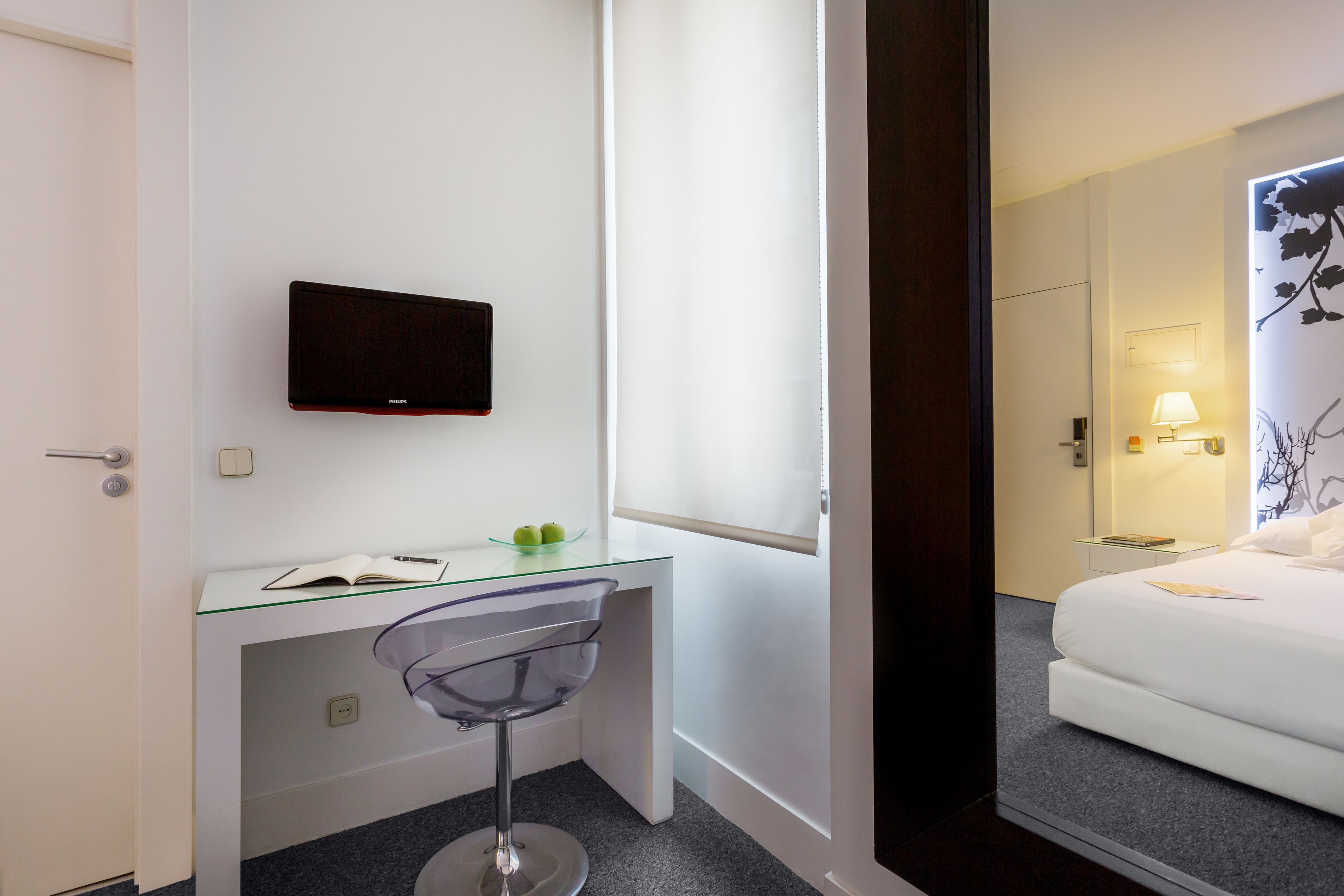 Una habitación de hotel con escritorio, silla, cama y televisor montado en la pared.