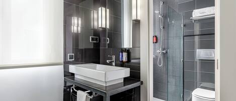 A modern bathroom with a white sink, dark tiles, a glass shower enclosure, and a white toilet.