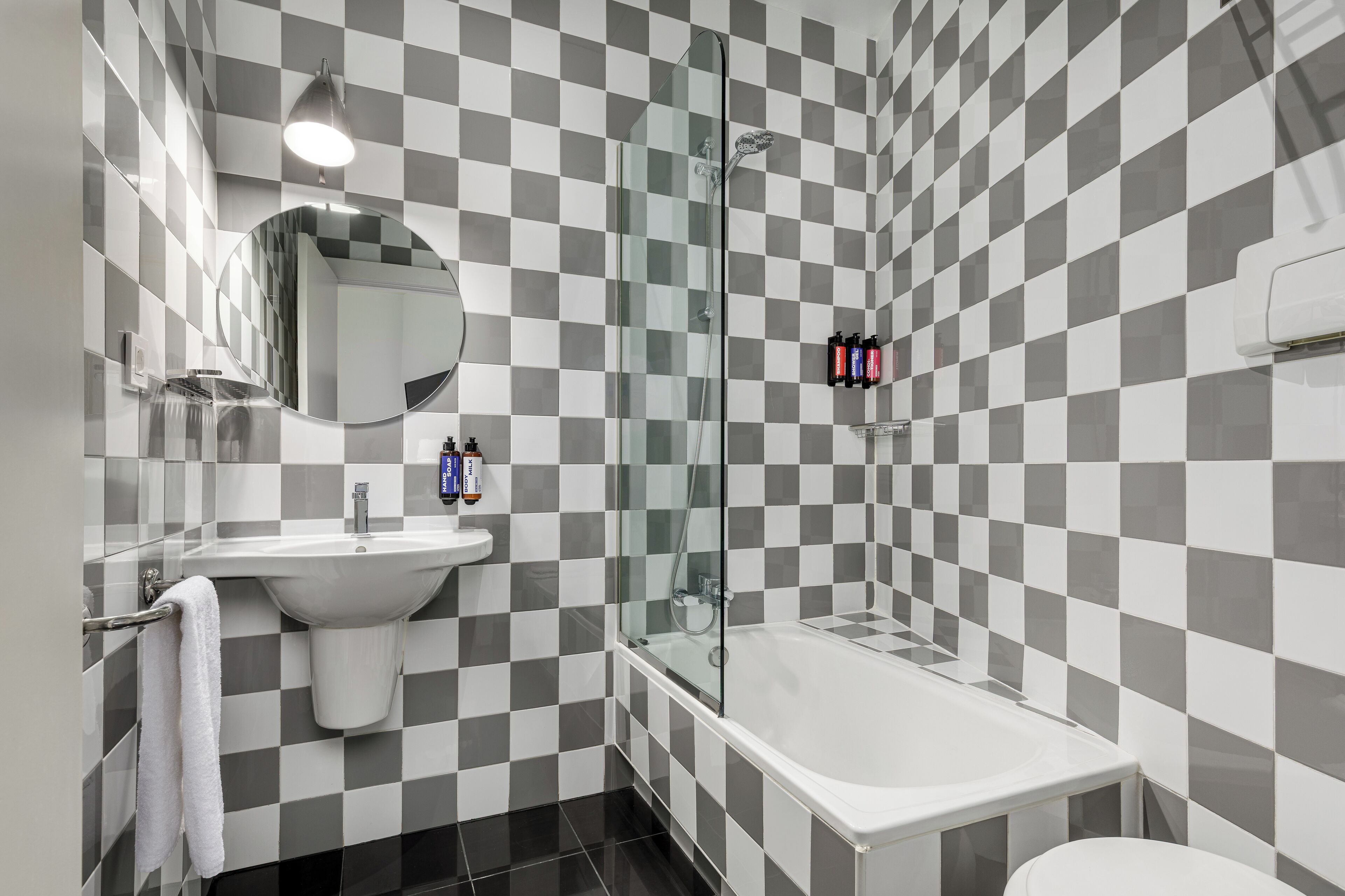 Une salle de bain avec un carrelage à motifs à carreaux, un lavabo, un miroir, une douche à parois de verre et une baignoire blanche.