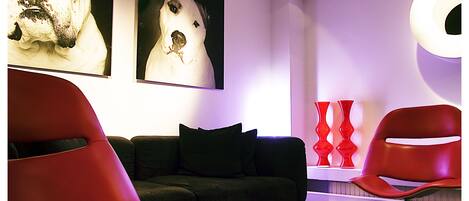 A modern living room with a black sofa, red chairs, and two large dog portraits on the wall.