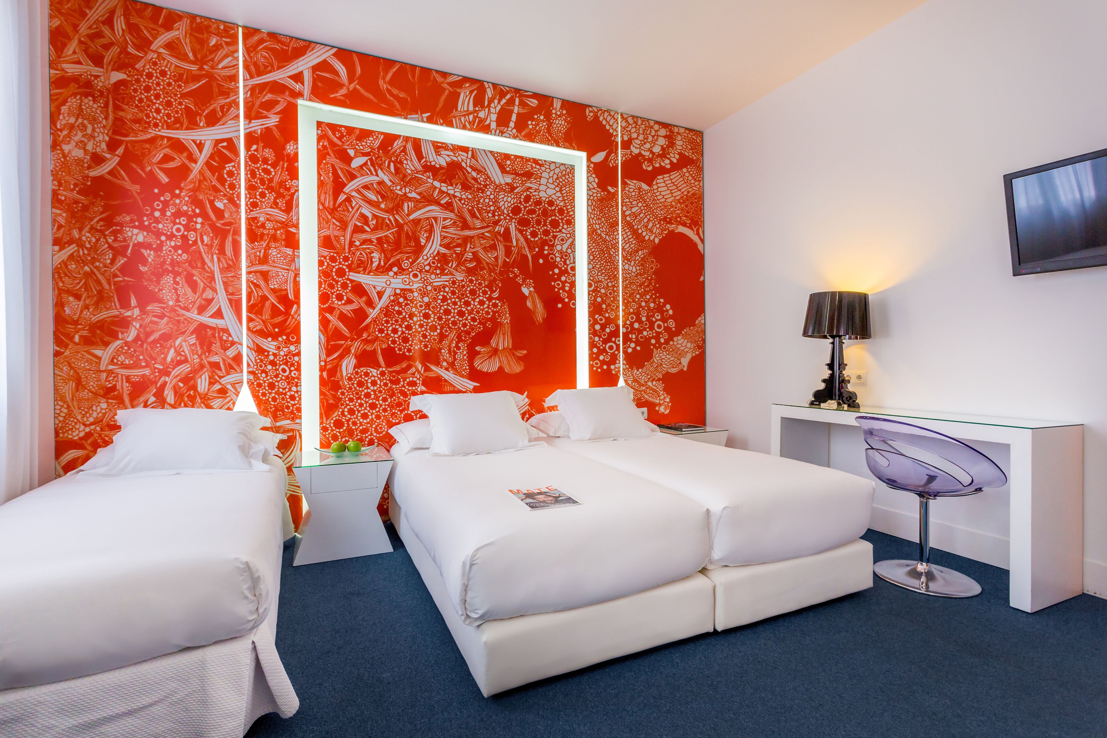 A hotel room with two beds, a desk, a chair, and a TV on the wall.
